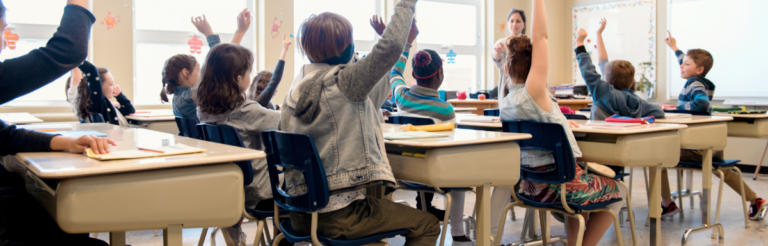 Students sit in class with arms raised